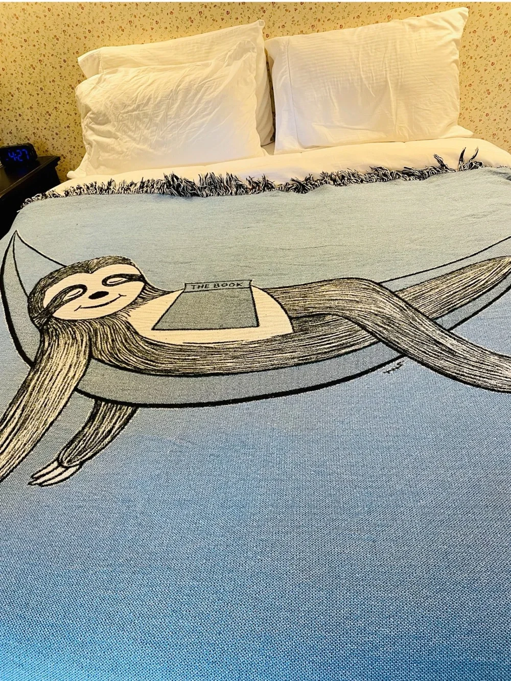 Outcasty cotton throw, relaxing sloth with book, shown on a Queen size bed
